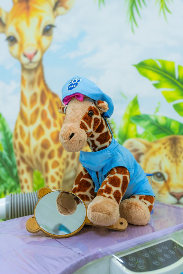 Jirafa de peluche vestida con gorro de dentista, sobre la bandeja del consultorio infantil